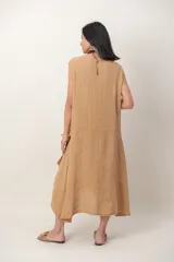 Vestido midi de lino color beige, sin mangas y con cuello redondo. Cuenta con un diseño irregular con detalle de volado vertical a un costado.