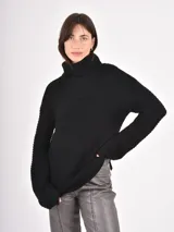 Buzo de tejido de punto grueso en color negro, con cuello alto tipo polera, mangas largas y corte holgado.