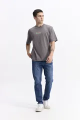 Remera de manga corta color gris oscuro con cuello redondo y ajuste regular. Presenta un estampado frontal con la palabra "BLESSED" en tipografía estilizada con tonos verde menta y rosado.