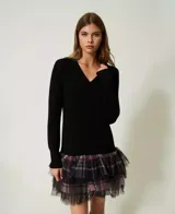 Vestido corto negro de punto liso con cuello en V y manga larga. Presenta capas de tul aplicado con estampado de cuadros multicolor.