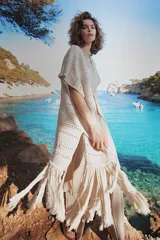 Chaleco largo de tejido de punto color azul verdoso, sin mangas y con flecos en el ruedo. Presenta calados con diseño geométrico.