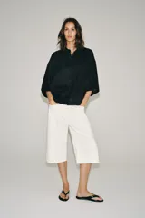 Camisa amplia confeccionada en hilatura con lyocell y ramio, color celeste, con cuello solapa, manga por debajo del codo, detalle de pliegue en la espalda y cierre frontal con botones ocultos por solapa.