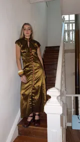 Vestido largo verde de tafeta con silueta entallada, cuello alto, mangas cortas, abertura tipo gota en el escote y hilera de botones frontal.