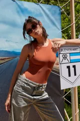 Body color marrón oscuro, confeccionado en microfibra, con escote delantero y trasero cerrado, cuerpo embolsado y gancho corsetero regulable en la entrepierna.