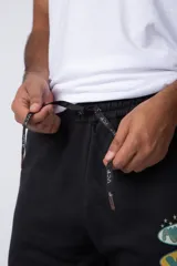 Pantalón jogger de corte oversize confeccionado en tela rústica color verde agua claro. Presenta una estampa gráfica localizada en el muslo izquierdo con diseño de óvalos y estrellas.