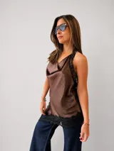 Blusa de inspiración lencera color marrón, con escote buche y detalles de encaje negro en los bordes. Presenta un diseño asimétrico con ruedo en pico y espalda descubierta.