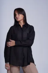 Camisa negra de tela traslúcida con cuello clásico, cierre frontal con botones y dos bolsillos de parche en el pecho.