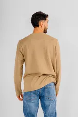 Buzo de manga larga con cuello redondo, confeccionado en tejido de punto con textura tipo waffle. Presenta un diseño minimalista con una pequeña etiqueta decorativa en el ruedo inferior.