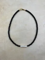 Collar artesanal compuesto por cuentas de piedra volcánica en diversos tonos y tamaños, con una perla natural de río como dije central y cierre metálico dorado.