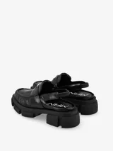 Mocasín mule de cuero negro con hebilla metálica y suela track.