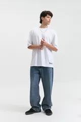 Remera oversize verde militar de manga corta y escote redondo, con estampado trasero de una cara sonriente amarilla con detalles en negro y texto "mistral 1976co".