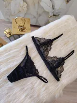 Conjunto de lencería compuesto por un bralette de encaje con breteles regulables y una tanga regulable con corte cola less. Ambas piezas presentan un diseño de encaje floral negro.