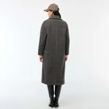 Abrigo largo de mujer, estilo lanoso, con estampado de pata de gallo o príncipe de Gales en tonos grises y marrones. Presenta un corte recto y holgado, cuello con solapas anchas y cierre cruzado con doble botonadura oscura.