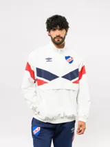 Buzo deportivo de nylon con medio cierre frontal, cuello alto y diseño con bloques de color blanco, azul y rojo. Presenta el logo de Umbro y el escudo del Club Nacional de Football en el pecho.