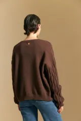 Cardigan de punto color terracota con diseño de trenzas verticales, cuello redondo y cierre frontal con botones metálicos. Presenta mangas largas con puños ajustados y un calce holgado.