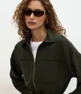 Campera tipo parka color verde oscuro, confeccionada en modal con cierre frontal metálico, cuello camisero, bolsillos frontales y cordón ajustable en la cintura.