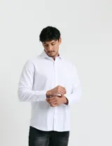 Camisa de vestir blanca de manga larga, con cuello clásico y cierre frontal de botones.