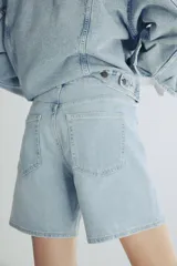 Short de media pierna en denim de algodón levemente elástico, de tiro alto con diseño de cinco bolsillos y cierre con botón.