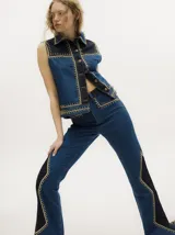 Pantalón de jean tiro alto con corte oxford, confeccionado en denim de algodón. Presenta un diseño bicolor con paneles laterales en tono más oscuro y detalles de apliques metalizados a lo largo de las costuras laterales y bolsillos.