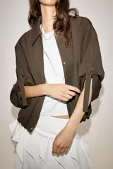 Chaqueta bomber color marrón, con cuello solapa, cierre frontal oculto con cremallera y botones a presión. Presenta mangas remangadas con trabillas y bajo abullonado con elástico interior.