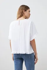 Blusa blanca de corte holgado con cuello redondo, mangas cortas con detalle de volados y ruedo con terminación de volado pequeño.