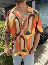 Camisa de manga corta con cuello cubano y cierre frontal de botones. Presenta un diseño estampado con formas geométricas abstractas en tonos cálidos y tierra.