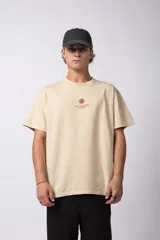 Remera de corte oversize color beige, confeccionada en algodón premium. Presenta un diseño minimalista con un pequeño estampado frontal de un sol y el texto 'VCP CONCEPT STUDIO' en color marrón.