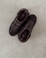 Zapatillas bajas de cuero vacuno color marrón chocolate, con cordones y detalle de flecos en el tobillo.