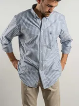 Camisa de corte regular confeccionada en algodón, con diseño de rayas verticales en azul y blanco. Presenta cuello abotonado, cierre frontal con botones, mangas largas y un bolsillo en el pecho con logo bordado.