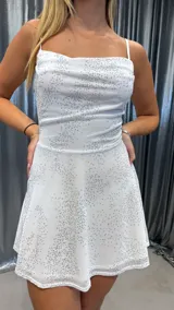 Vestido corto blanco con pequeños brillos plateados, escote drapeado, breteles finos y falda acampanada.
