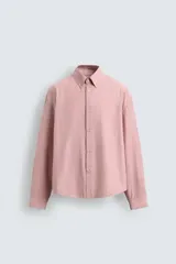 Camisa de corte relajado confeccionada en tejido de algodón, con diseño de rayas verticales en tonos rosados y blancos. Presenta cuello abotonado, cierre frontal de botones, manga larga con puños abotonados y bajo asimétrico.