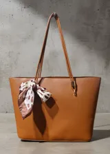 Cartera tipo tote bag color marrón, con diseño minimalista y textura granulada. Cuenta con doble asa larga y un pañuelo decorativo estampado con diseño de manchas atado en uno de los laterales.