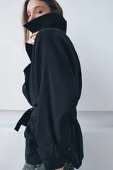 Trench corto de Zara, confeccionado en mezcla de lyocell, color verde militar. Presenta cuello solapa, manga larga con hombro caído y puños con trabilla. Incluye bolsillos delanteros de plastrón, cierre frontal cruzado con botón y cinturón de lazada en el mismo tejido.