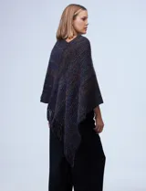 Poncho tejido en hilo soft, con efecto jaspeado multicolor (predominantemente tonos oscuros como azul marino, negro, y toques de violeta y dorado/lurex). Presenta un diseño asimétrico y flecos largos en los bordes.