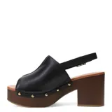 Sandalias de cuero negro con plataforma y taco cuadrado efecto madera. Presentan una tira frontal ancha con tachas metálicas decorativas y una pulsera ajustable con hebilla en el tobillo.