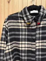 Camisa de franela escocesa en tonos bordó, negro y crudo, con cuello con pins sorpresa y cierre frontal oculto con botones.