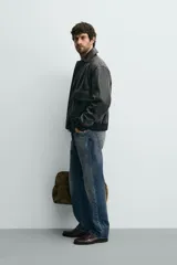 Cazadora relaxed fit de piel color marrón oscuro, con cuello solapa, manga larga y dos bolsillos plastrón con solapa en la cadera. Presenta detalle de bolsillo interior, efecto lavado y acabados en rib. El cierre frontal es con cremallera oculta por solapa con botones a presión.