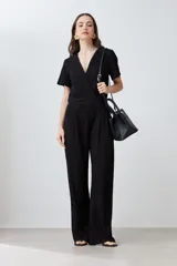 Mono largo negro con textura plisada, escote cruzado en V, mangas cortas con volados y pantalón palazzo.