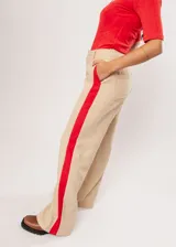 Pantalón beige de tiro alto con bolsillos delanteros y traseros, cierre frontal con cremallera y botón, y detalle de pespuntes rojos en los laterales.