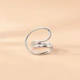 Anillo de plata 925 con diseño abierto de líneas curvas y envolventes que forman una estructura ancha y tridimensional.