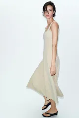 Vestido midi de color beige con escote cuadrado y tirantes anchos. Presenta un diseño entallado en el torso con costuras verticales marcadas y una falda con caída evasé.