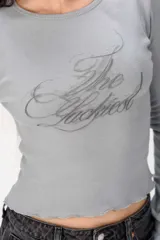 Remera de manga larga gris de corte ajustado, con cuello redondo y estampado frontal con la frase "The Luckiest".