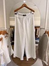 Pantalón blanco de tiro alto y corte amplio, confeccionado en Tencel y lino. Cuenta con bolsillos frontales tipo parche con solapa y un cinturón negro delgado incorporado.