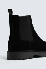 Bota tipo Chelsea de hombre con acabado en serraje, elásticos laterales y tirador trasero. Presenta horma redonda y suela track con volumen.