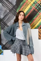 Saco de hilo con cuello alto y cierre de botones, de tejido de punto y diseño oversize. Presenta un teñido artesanal degradado que combina gris y beige, con mangas largas y puños amplios, además de un detalle de aplicación floral oscura en el pecho.