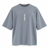 Remera oversize gris de manga corta, con cuello redondo y diseño gráfico estampado en tono beige en el frente y la espalda.