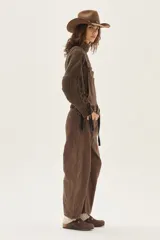 Overol de jean color marrón con calce barrel, tiro medio, pierna ancha y redondeada que termina a la altura del tobillo.