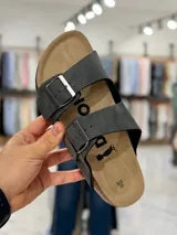 Sandalias de dos tiras negras con hebillas metálicas ajustables, plantilla anatómica y suela plana.
