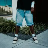Short de jean azul con diseño de strass aplicado en toda la prenda, formando motivos gráficos. Presenta ruedo desflecado y cierre frontal con botón.