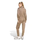 Conjunto deportivo Adidas Essentials Feel Cozy para mujer, compuesto por campera de cierre frontal con cuello alto y bolsillos laterales, y pantalón tipo jogger a juego. Presenta diseño liso en color marrón con el logo de la marca bordado discretamente en el pecho y en la pierna.